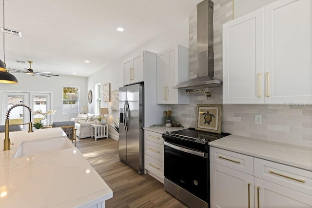 kitchen with white cabinets, hanging light fixtures, stainless steel appliances, light stone countertops, and wall chimney range hood