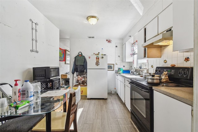 kitchen featuring tasteful backsplash, light hardwood / wood-style floors, white cabinets, black / electric stove, and white fridge