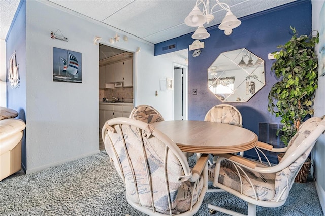 carpeted dining room featuring a notable chandelier, visible vents, and a sink