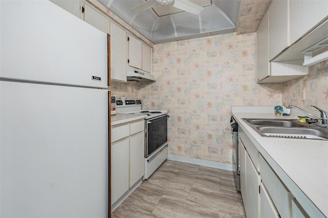 kitchen featuring a sink, baseboards, under cabinet range hood, wallpapered walls, and white appliances