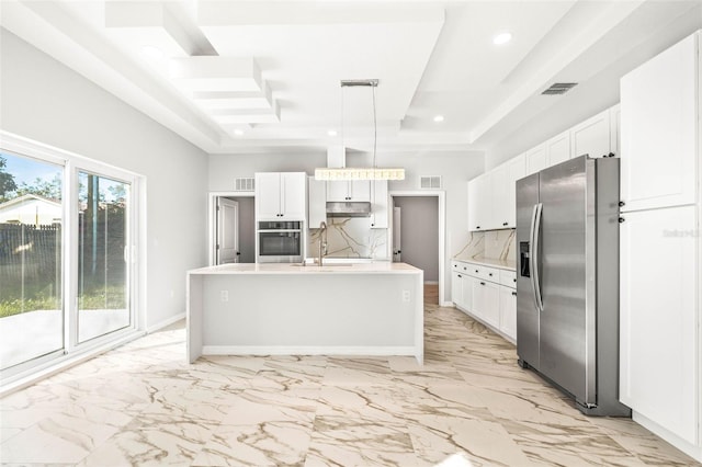 kitchen with decorative backsplash, stainless steel appliances, a raised ceiling, decorative light fixtures, and a center island with sink