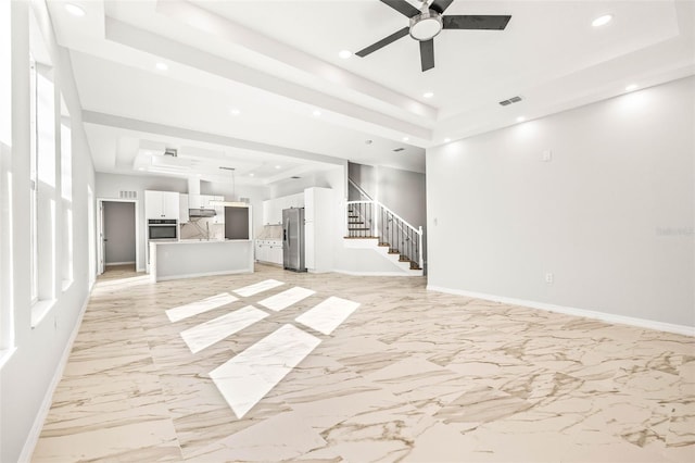 unfurnished living room featuring ceiling fan and a tray ceiling