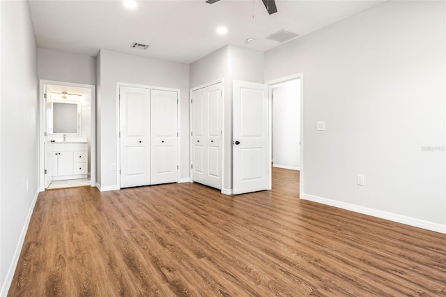 unfurnished bedroom featuring ensuite bath, ceiling fan, multiple closets, and hardwood / wood-style flooring