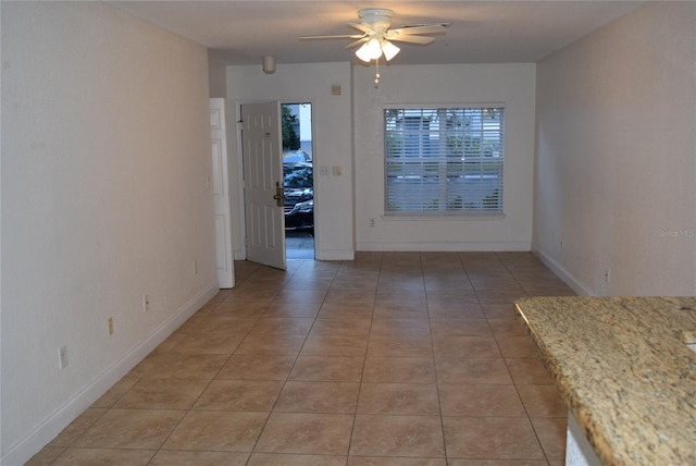 unfurnished dining area featuring a ceiling fan, baseboards, and light tile patterned floors