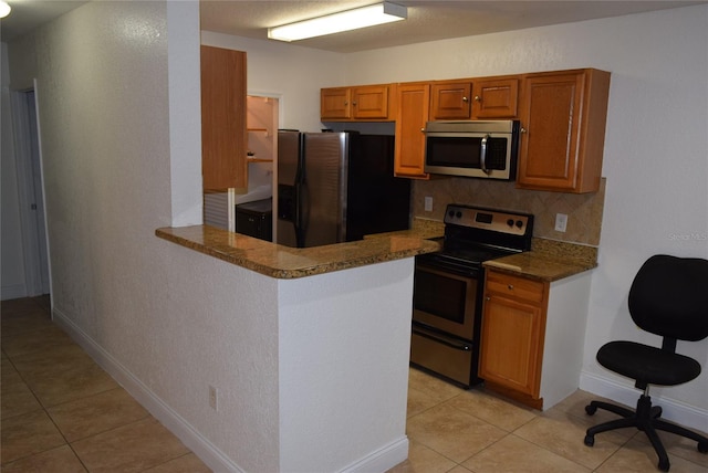 kitchen with baseboards, appliances with stainless steel finishes, brown cabinets, backsplash, and light tile patterned flooring