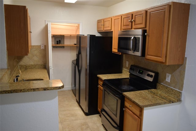 kitchen featuring light tile patterned floors, stainless steel appliances, a sink, tasteful backsplash, and brown cabinetry