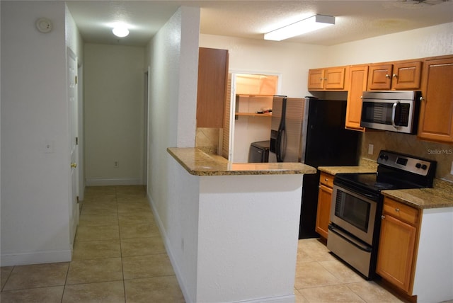 kitchen featuring light tile patterned floors, washer and clothes dryer, appliances with stainless steel finishes, a peninsula, and backsplash