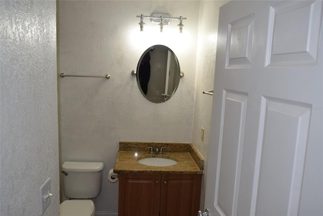 bathroom with a textured wall, vanity, and toilet