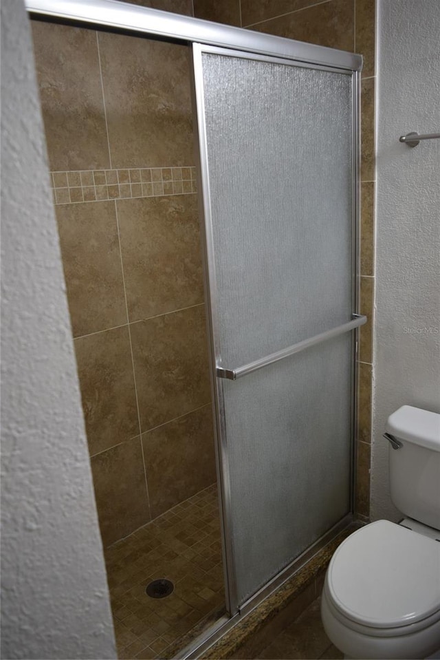 bathroom featuring a textured wall, a stall shower, and toilet