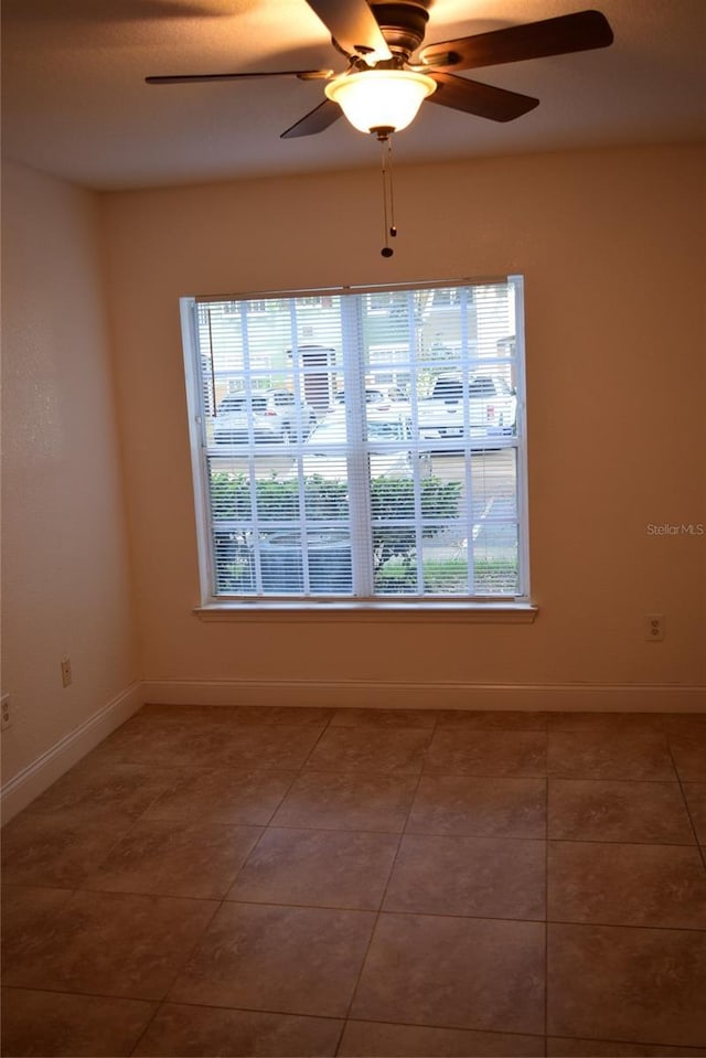 tiled spare room with a wealth of natural light, ceiling fan, and baseboards