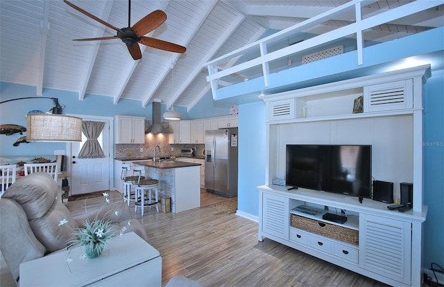 living room featuring high vaulted ceiling, sink, ceiling fan, light wood-type flooring, and beam ceiling