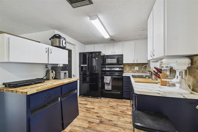 kitchen with wood counters, sink, blue cabinetry, black appliances, and white cabinetry