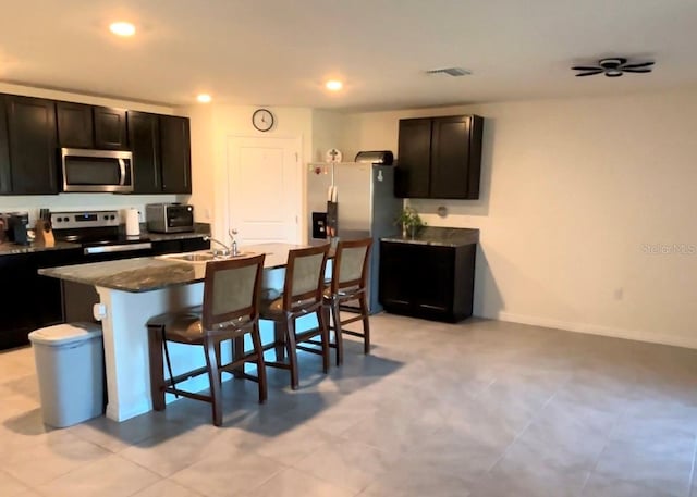 kitchen with a kitchen bar, appliances with stainless steel finishes, dark stone counters, sink, and a kitchen island