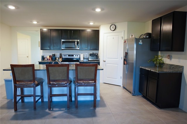 kitchen with appliances with stainless steel finishes, a kitchen island with sink, a breakfast bar area, and dark stone countertops