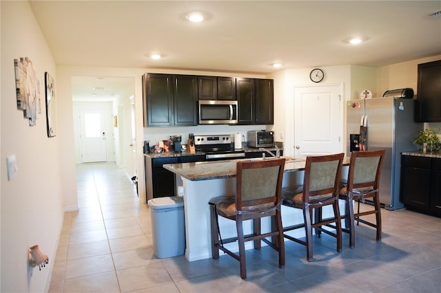 4694 Sigcom Pl, Wildwood, FL 34785 - kitchen featuring appliances with stainless steel finishes, a kitchen bar, light tile patterned flooring, an island with sink, and recessed lighting