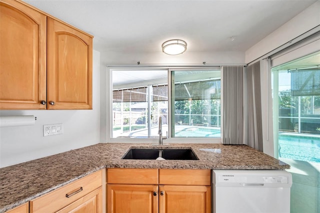 kitchen featuring light brown cabinets, white dishwasher, light stone counters, and sink