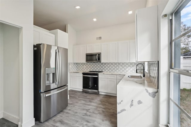 kitchen with white cabinets, sink, decorative backsplash, light stone countertops, and stainless steel appliances