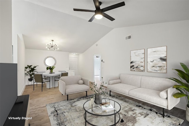 living room featuring ceiling fan with notable chandelier, light hardwood / wood-style floors, and vaulted ceiling