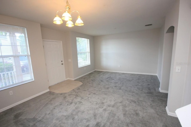 spare room with carpet flooring, a notable chandelier, and a healthy amount of sunlight