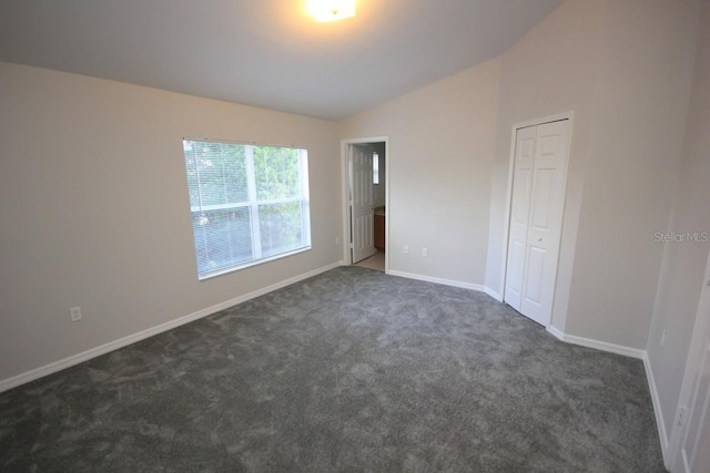 unfurnished bedroom with dark carpet, a closet, and lofted ceiling