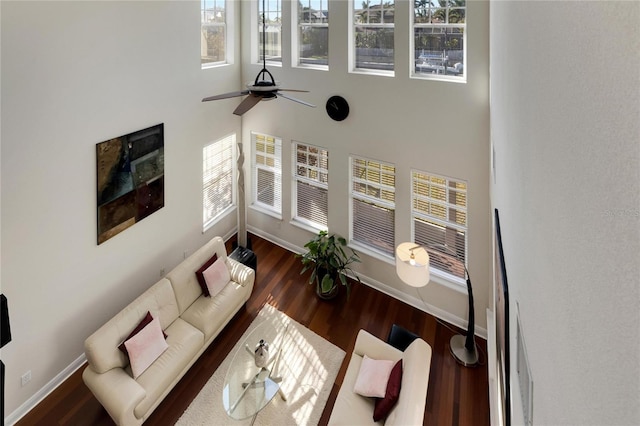 living room with ceiling fan, a towering ceiling, and dark wood-type flooring