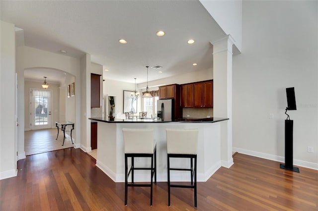 kitchen featuring kitchen peninsula, stainless steel refrigerator with ice dispenser, decorative backsplash, dark hardwood / wood-style floors, and hanging light fixtures