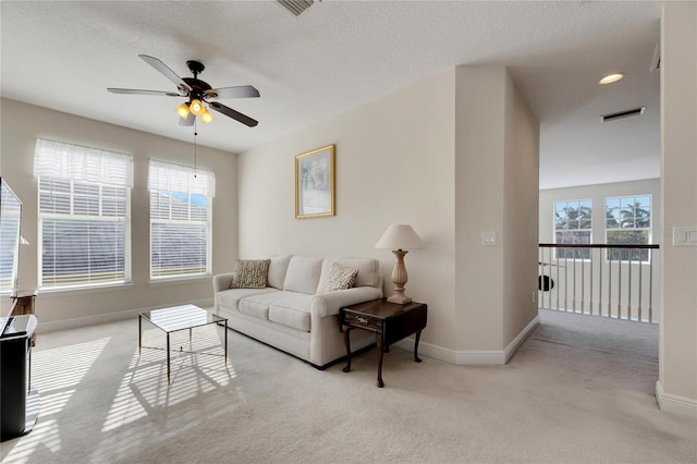 living room featuring ceiling fan, light colored carpet, and a textured ceiling