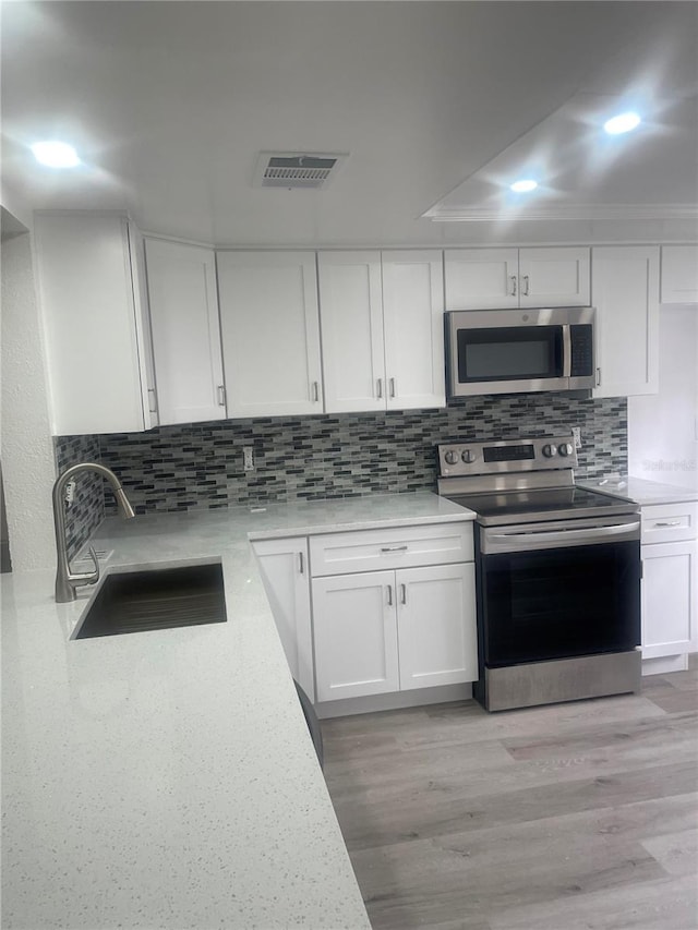 kitchen featuring tasteful backsplash, stainless steel appliances, sink, light hardwood / wood-style flooring, and white cabinets