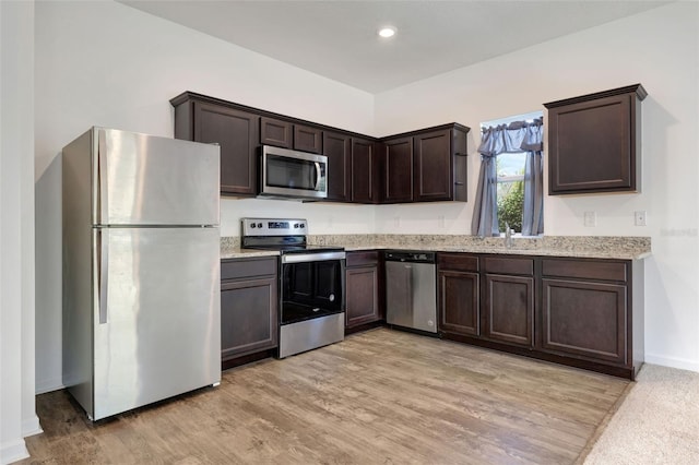 kitchen featuring sink, light stone counters, dark brown cabinets, appliances with stainless steel finishes, and light wood-type flooring