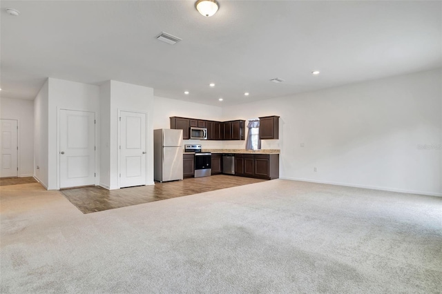 kitchen with dark brown cabinetry, light carpet, and stainless steel appliances