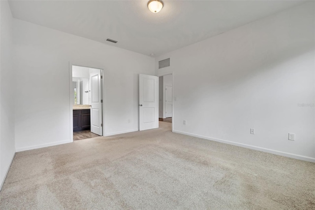 unfurnished bedroom featuring light colored carpet and ensuite bath