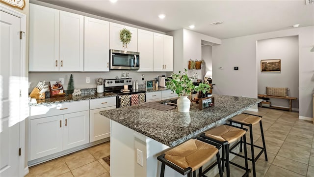 kitchen featuring dark stone counters, stainless steel appliances, a center island, white cabinetry, and a breakfast bar area