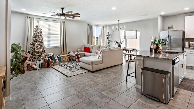 living room with a textured ceiling, ceiling fan with notable chandelier, light tile patterned floors, and sink