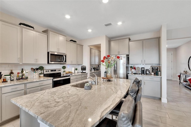 kitchen featuring a center island with sink, light stone counters, sink, and stainless steel appliances