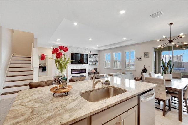 kitchen with stainless steel dishwasher, a raised ceiling, light stone countertops, and sink