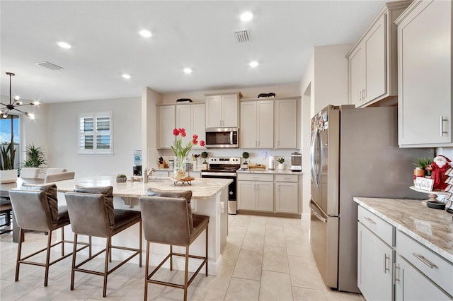 kitchen featuring appliances with stainless steel finishes, decorative light fixtures, light stone counters, and a center island with sink