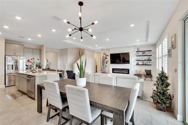 tiled dining area featuring a tray ceiling, a stone fireplace, sink, and a chandelier