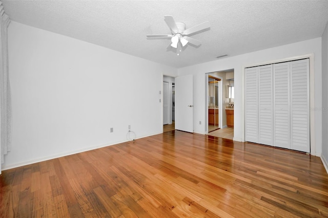 unfurnished bedroom with ceiling fan, hardwood / wood-style flooring, ensuite bath, and a textured ceiling