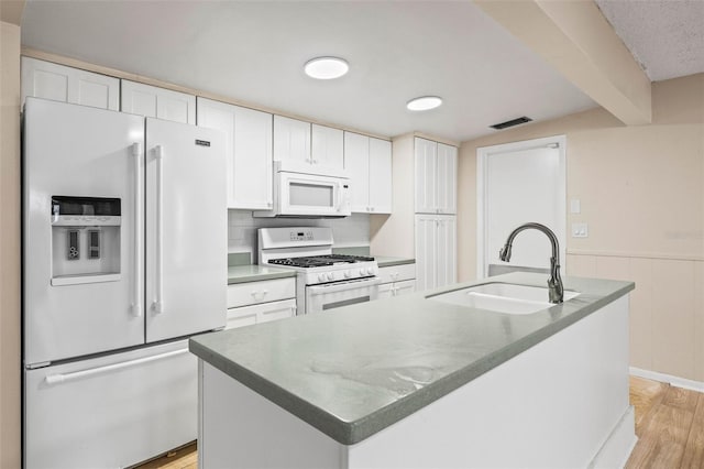 kitchen featuring white cabinets, a center island with sink, white appliances, and sink