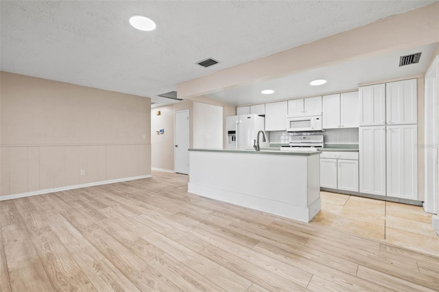 kitchen featuring white cabinetry, light wood-type flooring, white appliances, and a kitchen island with sink