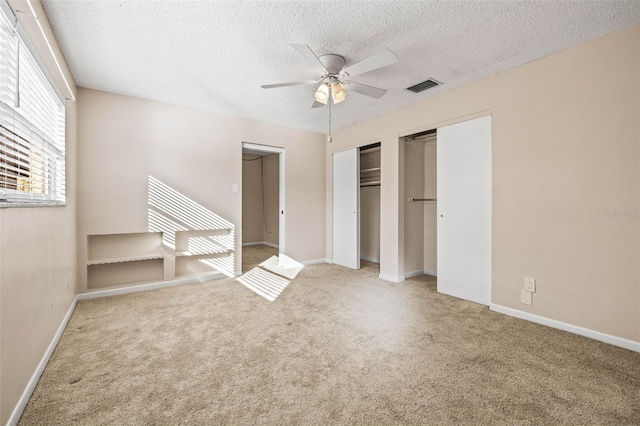 unfurnished bedroom with ceiling fan, carpet floors, a textured ceiling, and two closets