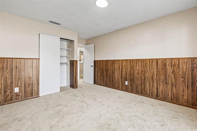 unfurnished bedroom featuring carpet flooring, wood walls, a closet, and a textured ceiling