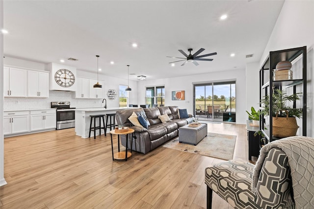 living room featuring light wood-type flooring, ceiling fan, and sink