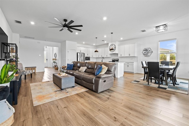 living room with ceiling fan, sink, and light wood-type flooring