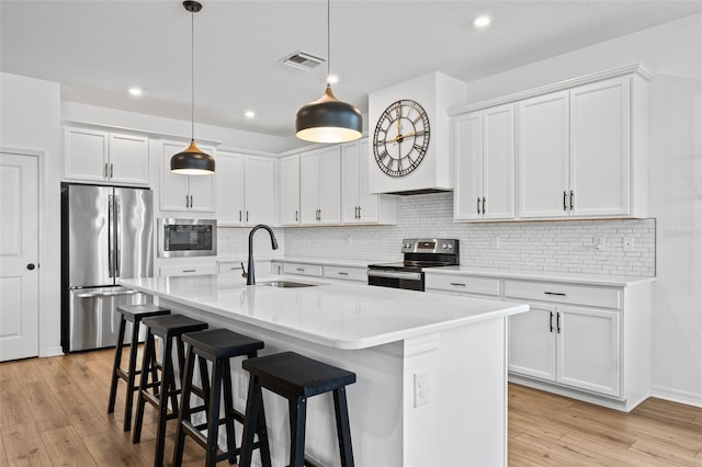 kitchen featuring white cabinets, a kitchen island with sink, sink, and appliances with stainless steel finishes