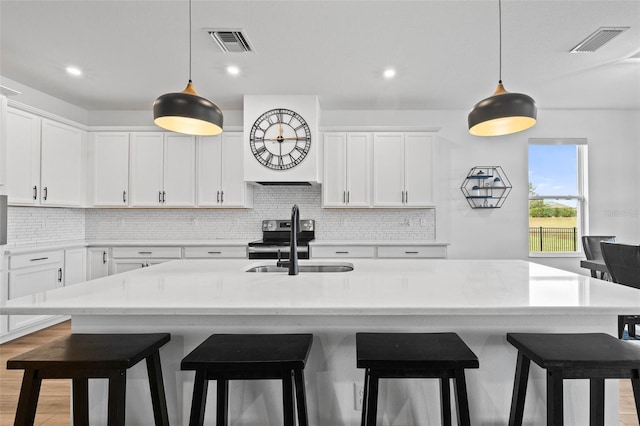 kitchen with white cabinetry, sink, a breakfast bar area, and an island with sink