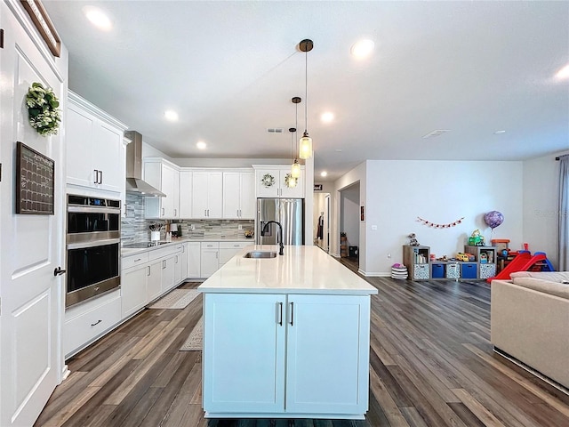 kitchen featuring a kitchen island with sink, sink, wall chimney exhaust hood, white cabinetry, and stainless steel appliances