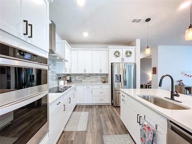 kitchen featuring white cabinetry, sink, hanging light fixtures, stainless steel appliances, and wall chimney range hood