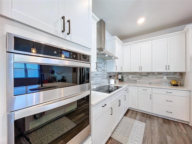 kitchen with wall chimney exhaust hood, stainless steel double oven, backsplash, black electric cooktop, and white cabinets