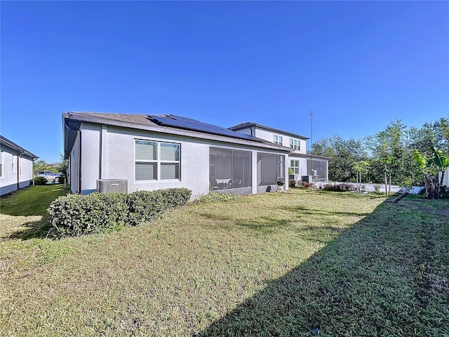 back of property with a sunroom, a yard, central AC unit, and solar panels